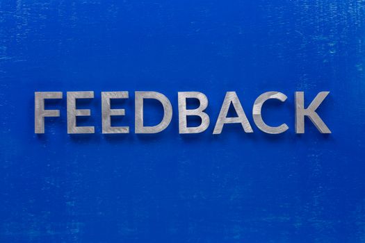 The word feedback laid on blue painted board with thick silver metal aphabet characters., centered composition concept