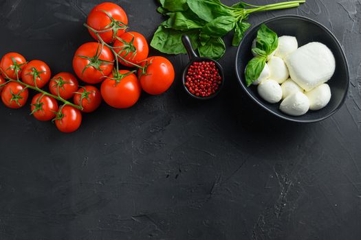 Mozzarella cheese balls, cherry tomatoes and green fresh organic basil italian cuisine . Ingredients for caprese Organic Mediterranean food concept, flat lay top view space for text. Black table.