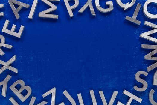 Frame mockup made of of silver metal english alphabet characters on blue background. Usable for back to school or language education projects.