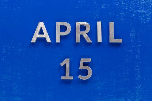 the words april 15 layed on blue painted board with thick silver metal aphabet characters - directly above flat lay composition reminder