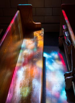 Wooden bench pews illuminated by light from stained glass window
