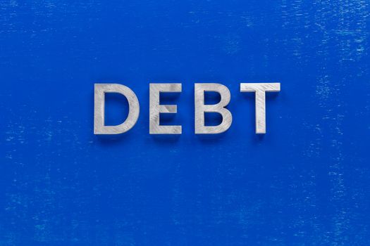 the word debt layed on blue painted board with thick silver metal aphabet characters, centered composition