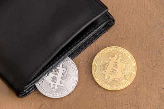 Two cryptocurrency Bitcoin metallic coins coming out a leather wallet