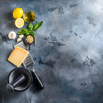 Different ingredients for Italian pesto. On the stone table cooking ingredients on dark background with Parmesan cheese, basil leaves, pine nuts, olive oil, garlic, salt and pepper. Layout with free text space