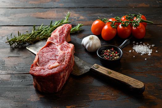 Raw Spencer steak on meat cleaver. Organic farm marbled prime black angus beef. Dark wooden background. Side view. With seasonings, peppercorns, rosemary,salt,garlic. close up noone
