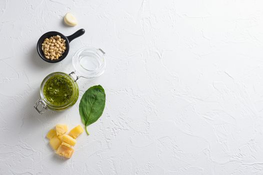 Green Pesto Basil Sauce in glass jar . with ingredients parmesan basil pine nuts on white background top view lay flat space for text.