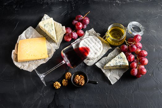Grapes, red wine, cheeses, brie cheese , blue, chease honey and nuts over black background top view.