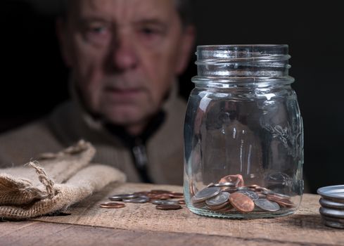 Senior man or retiree looking at glass savings jar in depression as he sees how little money is left