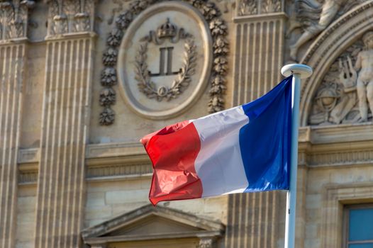 French flag waving in front of the facade of the Louvre Museum in Paris