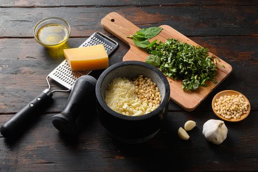 Pesto sauce cooking and mortar with ingredients . Basil, olive oil, parmesan, garlic, pine nuts. Top view on old vintage wooden table side view .