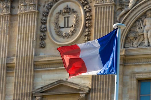 French flag waving in front of the facade of the Louvre Museum in Paris