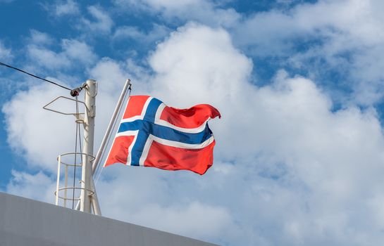 Flag of norway flying from the mast of a cruise ship against a blue sunny sky