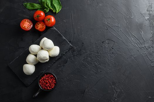 Fresh cherry tomatoes, basil leaf, mozzarella cheese on black slate stone chalkboard Healthy Italian traditional caprese salad ingredients. Organic Mediterranean food concept, flat lay space for text.