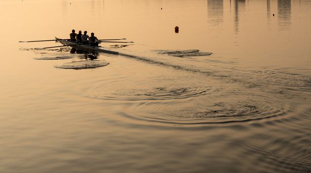 Sunrise lights up team of four rowers in canoe practicing in London Docklands