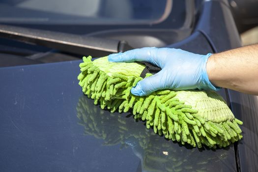 Domestic work: woman clean blue car in green glowes with sponge in hand