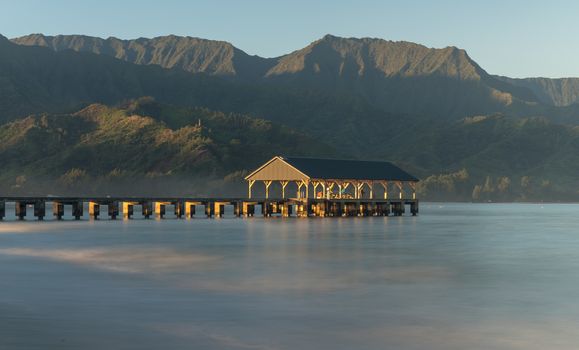 Sunrise lights the dawn sky above Hanalei Pier with the Na Pali coast in the background near Hanalei, Kauai, Hawaii