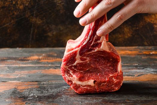 Raw tomahawk steak in butcher hands side view over rustic old cutting board with dark planks.