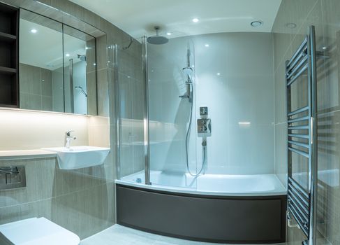 Modern clean bathroom in flat or apartment with bath shower, towel rail, sink and mirror cabinets