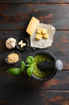 fresh Green basil pesto preparation in black mortar with italian recipe ingredients over old wood table copy space for text overhead.