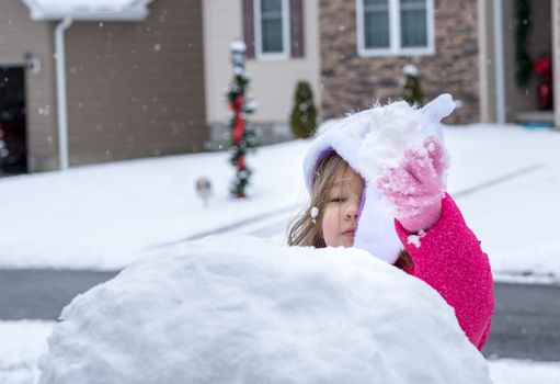 Young toddler girl playing in the snow and making a snowman