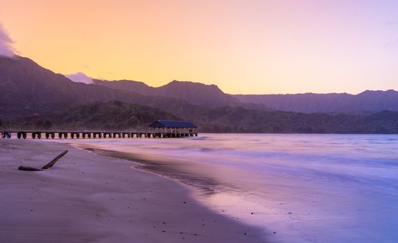 Sunrise lights the dawn sky above Hanalei Pier with the Na Pali coast in the background near Hanalei, Kauai, Hawaii