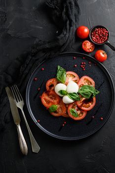 Tomato, basil, mozzarella Caprese salad with balsamic vinegar and olive oil. Top view, blkack stone background overhead.