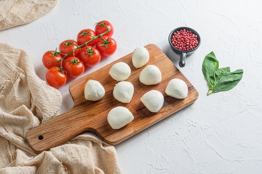 Mini balls of mozzarella cheese, on chop wood board ingredients for salad Caprese. over white background. Top view.