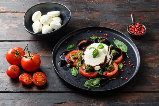 Italian food - caprese salad with sliced tomatoes, mozzarella cheese, basil, olive oil. Served on black plate over dark wood background. Top view. Rustic style