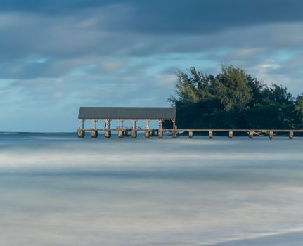 Sunrise lights the dawn sky above Hanalei Pier with long duration exposure to blur waves near Hanalei, Kauai, Hawaii
