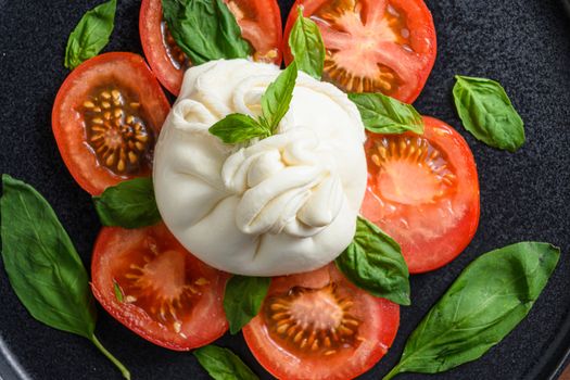 Handmade burrata cheese served with fresh tomatoes and basil leaves traditional italian Salad close up top view.