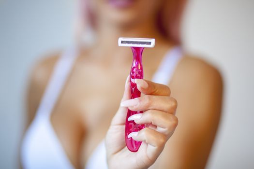 Attractive pink hair young woman hold and showing shaver razor for epilation hair removal with ergonomic pink holder. Body care skincare beauty concept