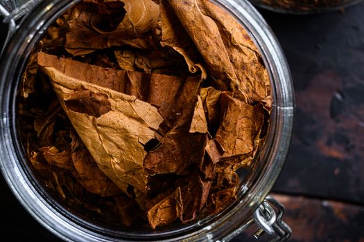 close-up Cigar and pile of tobacco leaves of Dried tobacco in glass jars on rustic wood dark table top view overhead.