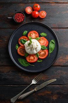 Burrata, Italian fresh cheese made from cream and milk of buffalo or cow. on black plate old wood table planks top view.