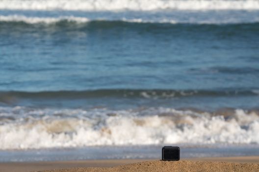 Focus on camera taking video or timelapse footage from sandy beach towards rolling surf and waves