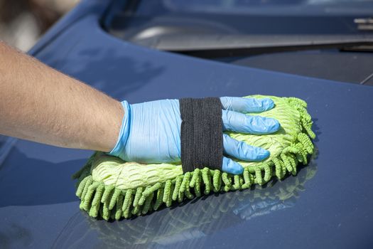 Domestic work: woman clean blue car in green glowes with sponge in hand