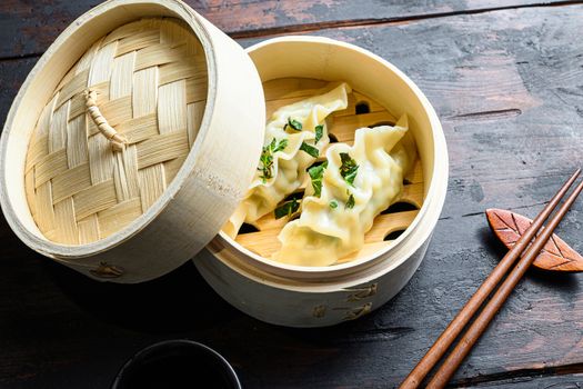 Gyozas potstickers chinese dumplings in wooden steamer with soy sauce fresh herbs and chopsticks on old wood table side view close-up.