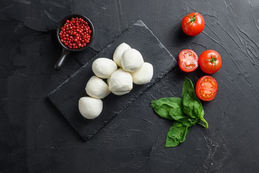 Mozzarella cheese, basil tomato cherry over old black backgroundon black stone slate space for text.