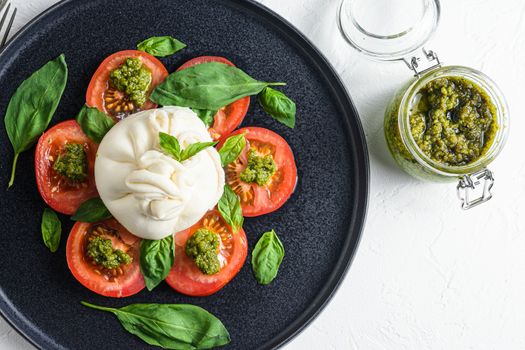 burrata Buffalo cheese served with fresh tomatoes and basil leaves pesto sauce on black plate white background flatlay .