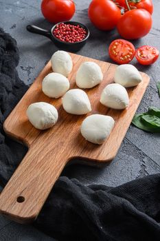 Buffalo Mozzarella cheese balls with fresh basil leaves and cherry tomatoes, the ingredients of the Italian Caprese salad, on a black cloth and grey concrete background close up vertical.