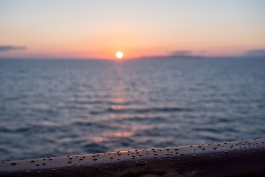 Water droplets on teak rail of small cruise liner sailing across the ocean as sun rises