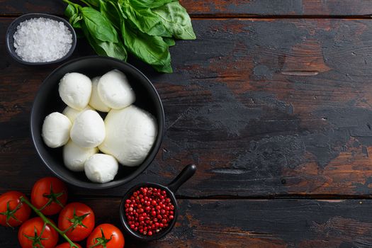 Raw ripe Mozzarella cheese balls with fresh basil leaves and cherry tomatoes, the ingredients , on old wood background top view space for text.