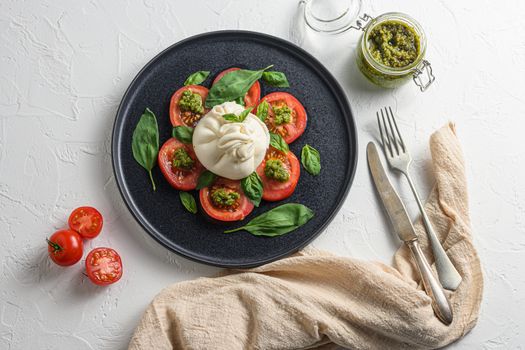 Salad with traditional italian burrata cheese made from cream and milk of buffalo or cow on black flat plate top view flatlay white concrete background cloth and old fork and knife.