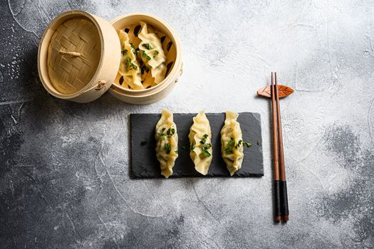 Boiled and hot chinese dumplings in wooden steamer and on black stone board slate over grey stone textured table background top view.