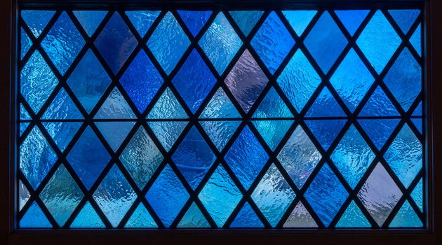 Detail of blue diamond shaped panes in colored light from stained glass window in catholic church