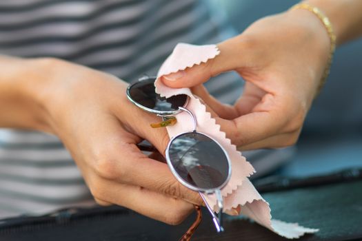 Woman hands cleaning her sun glasses with micro fiber cloth wipe, wiping sunglasses