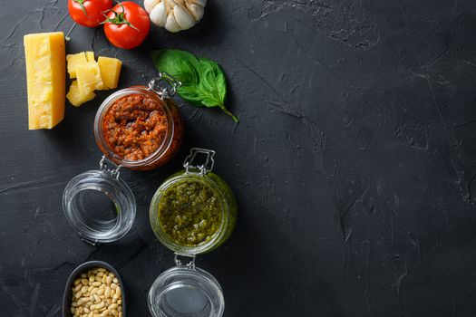 red and green Pesto alla Genovese , Basil Sauce resh home made and cooking italian recipe ingredients Parmesan cheese, basil leaves, pine nuts, olive oil, garlic, salt, tomatoes chulkboard top view on black stone concrete surface space for text.