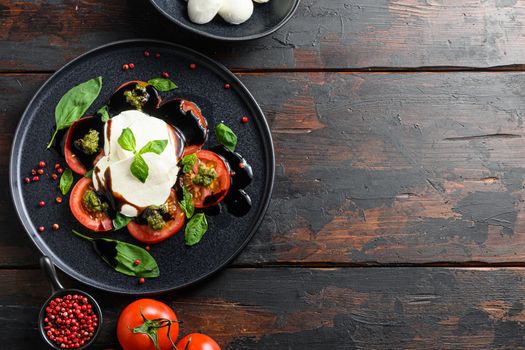 Italian food - caprese salad with sliced tomatoes, mozzarella cheese, basil, olive oil. Served on black plate over dark wood background. Top view. Rustic style. space for text layflat.