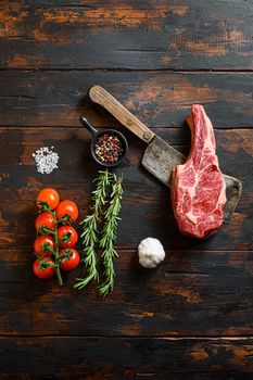 Fresh Cowboy steak cut on meat cleaver. Organic farm marbled prime black angus beef. Dark wooden background. Top view. With seasonings, peppercorns, chilie, rosemary,salt,garlic. Copy space. Vertical