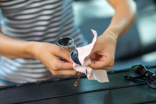 Woman with hands cleaning her sun glasses with micro fiber cloth wipe, wiping sunglasses