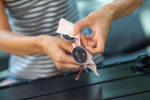 Woman hands cleaning her sun glasses with micro fiber cloth wipe, wiping sunglasses